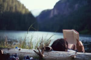 person reading a book near a lake